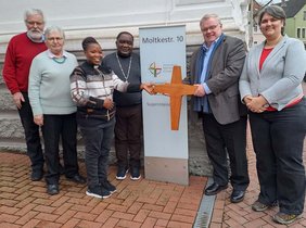 Das Altarkreuz aus der Christuskirche in Stromberg – die Kirche wurde im Sommer 2024 geschlossen – findet eine neue Heimat in der Diözese Karagwe, Tansania. Superintendent Frank Schneider (2.v.r.) überreicht es den Gästen Deogratias Aberatha Kokuberwa (3.v.l.) und Benson Boganza bei ihrem Besuch in Gütersloh. Pfarrer Ulrich Klein (links), Christa Marienhagen (2.v.l.) und Maxie Kordes (rechts). 	Foto: KKGT