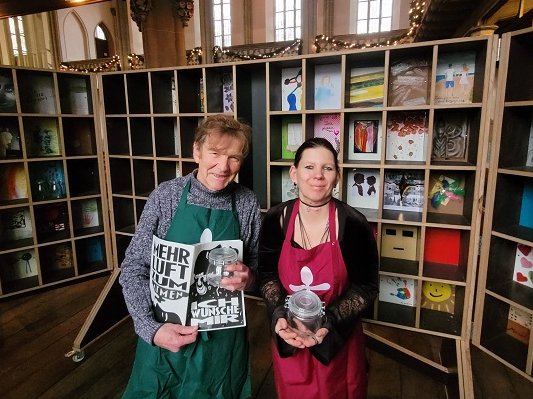 Reinhard Michel und Vanessa Henkelmann begleiten die Kunstaktion. In ihren Händen halten sie Weckgläser, die ab Samstag in der Martin-Luther-Kirche abzuholen sind. Michel und Henkelmann stehen vor dem Regal, das als Suppenregal entstand und im vergangenen Jahr zu einer „Wunschkammer“ wurde. Aus den Wünschen, die die Gütersloher während der Vesperkirche und im Mai während der „langenachtderkunst“ in dieser Kammer hinterließen, ist ein Heft entstanden, gestaltet von Lara Kees. Gedruckt und gebunden, ist es während der Vesperkirche 2026 zu bekommen. Foto: privat